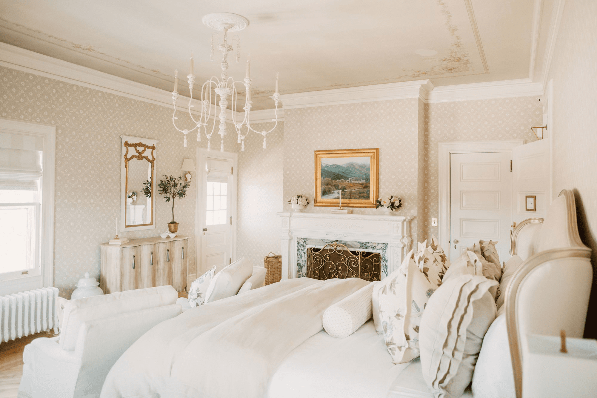 A elegantly styled bedroom featuring a chandelier, plush bedding, and tasteful artwork.