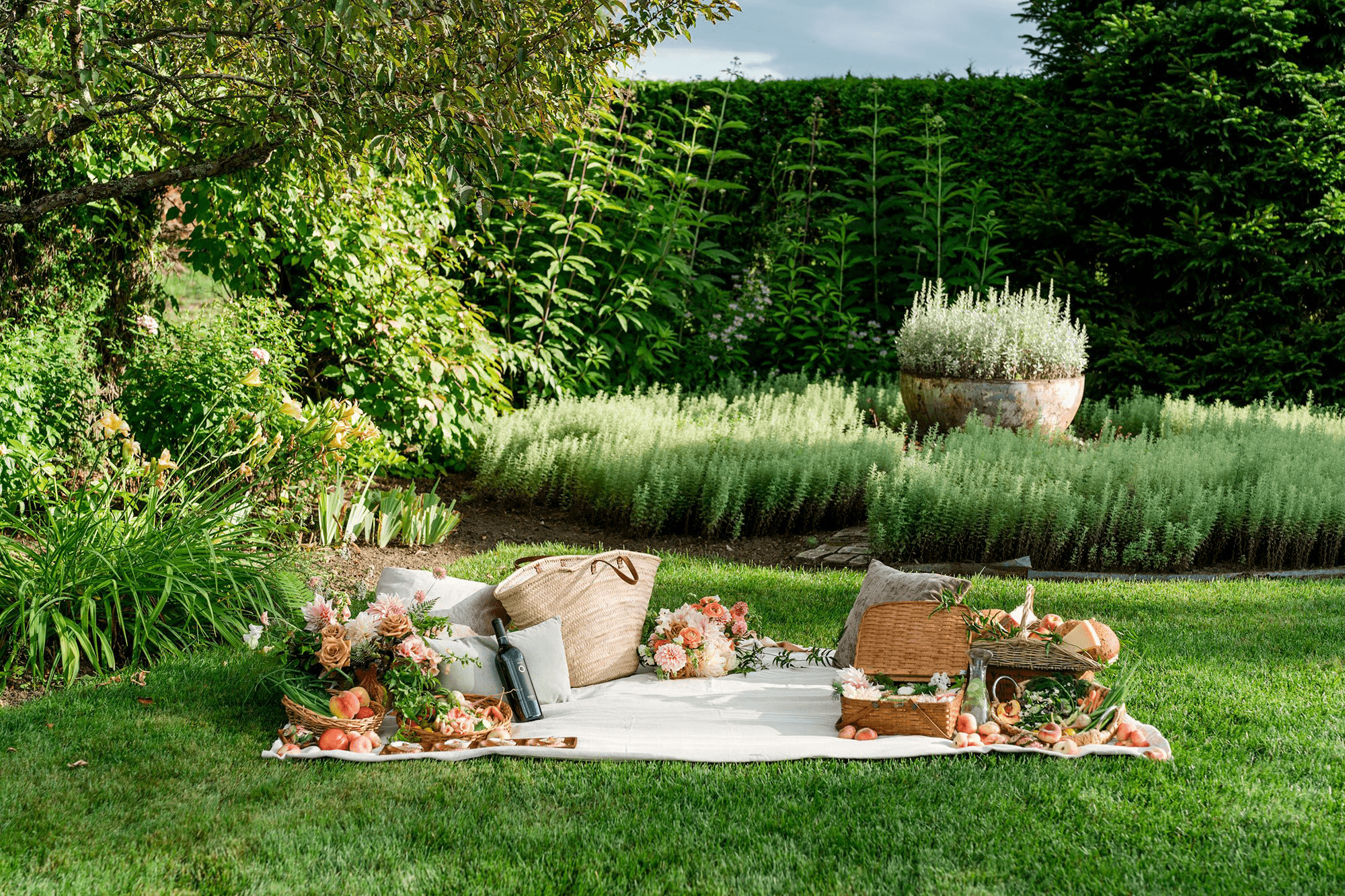 A beautifully arranged picnic setup in a lush garden, featuring baskets, flowers, and a cozy blanket.