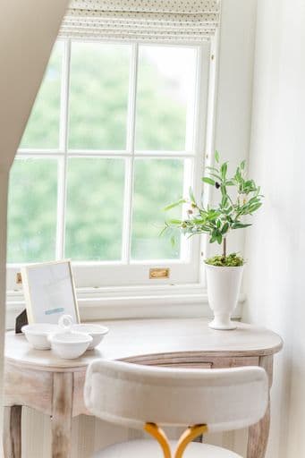 A bright, minimalist workspace featuring a wooden desk, potted plant, and window with natural light.
