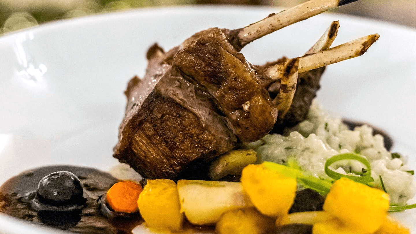 A beautifully plated rack of lamb with risotto and colorful vegetables.