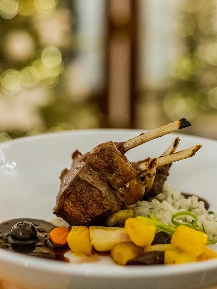 A beautifully plated dish featuring lamb chops atop creamy risotto, garnished with colorful vegetables and a drizzle of sauce.