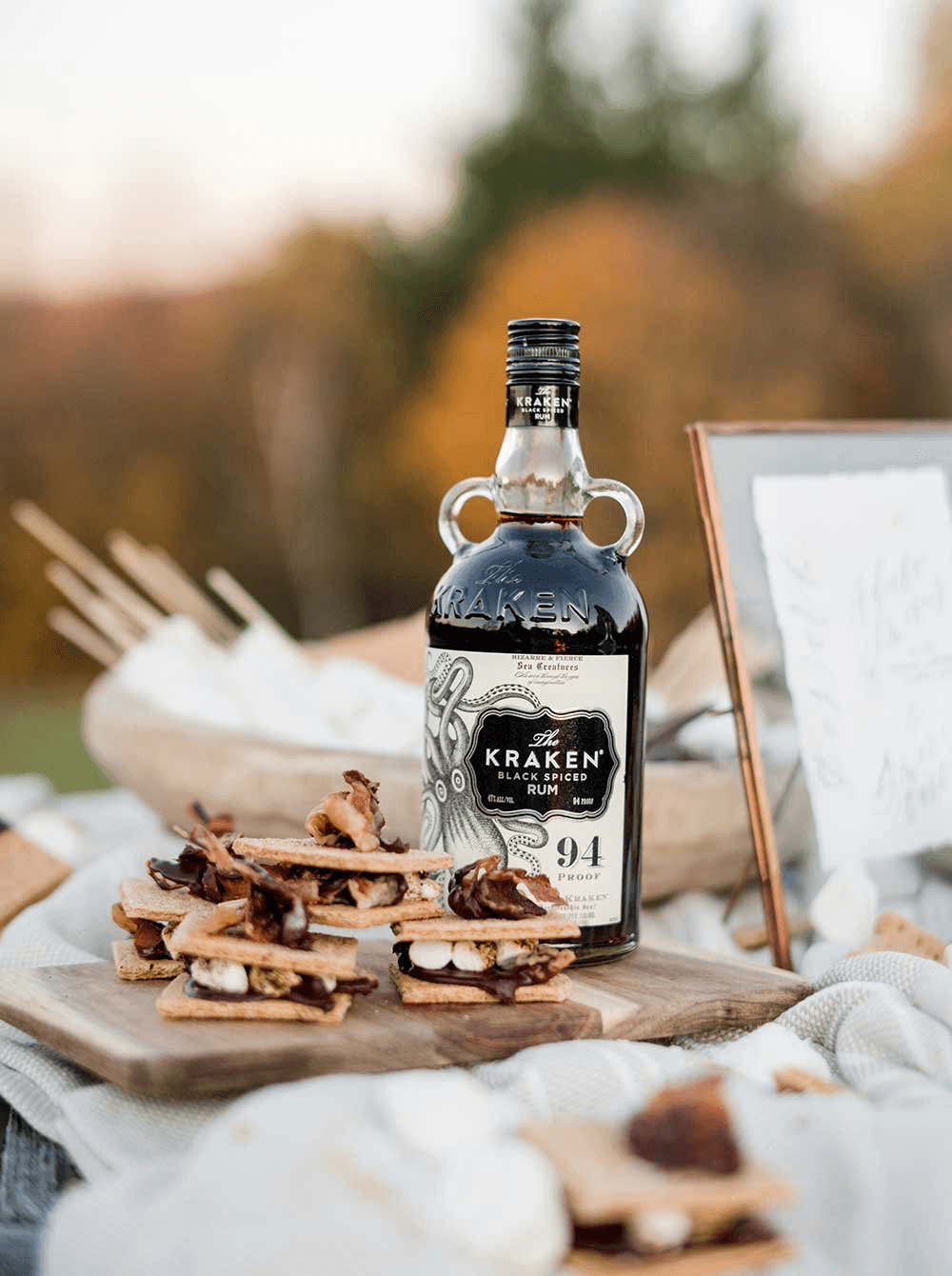 A bottle of Kraken Black Spiced Rum sits among a rustic spread of snacks.