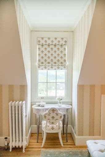 A cozy corner showcasing a small round table with a vase and a decorative chair next to a window with patterned shades.