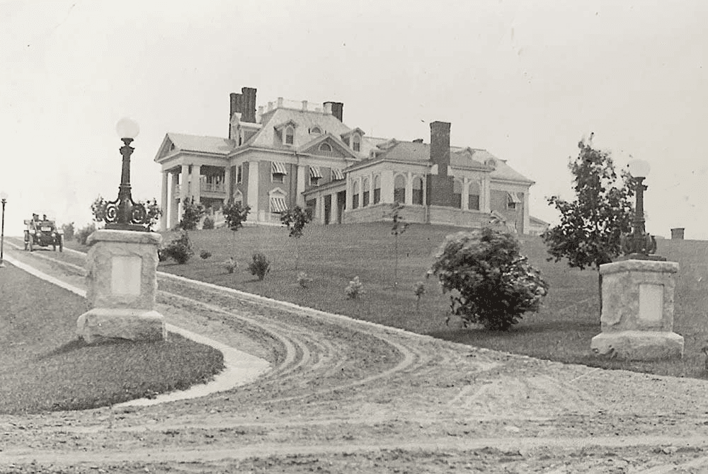 Historic mansion with ornate architecture and lampposts set on a grassy hill.