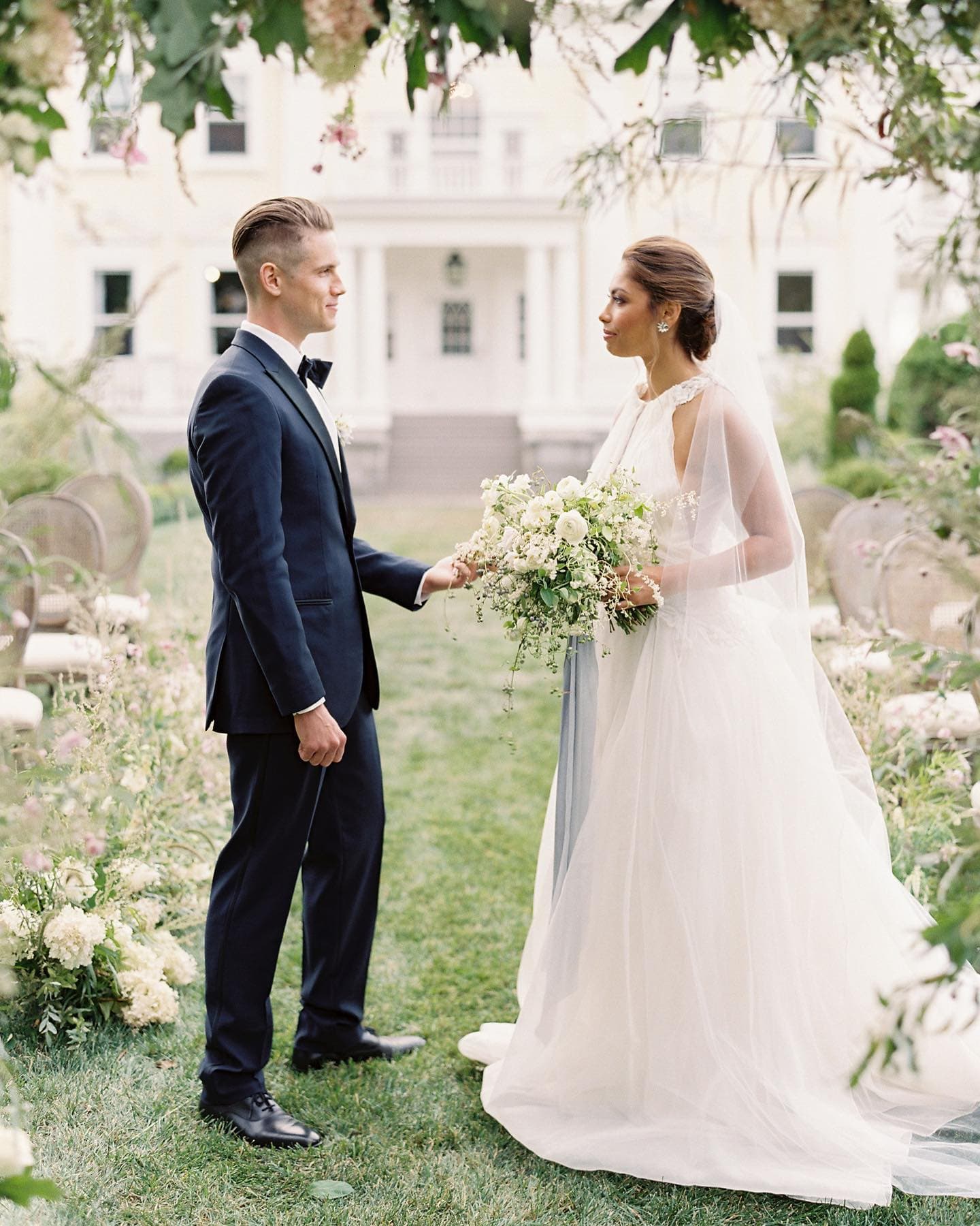 A couple exchanges vows surrounded by floral decorations in a serene outdoor setting.
