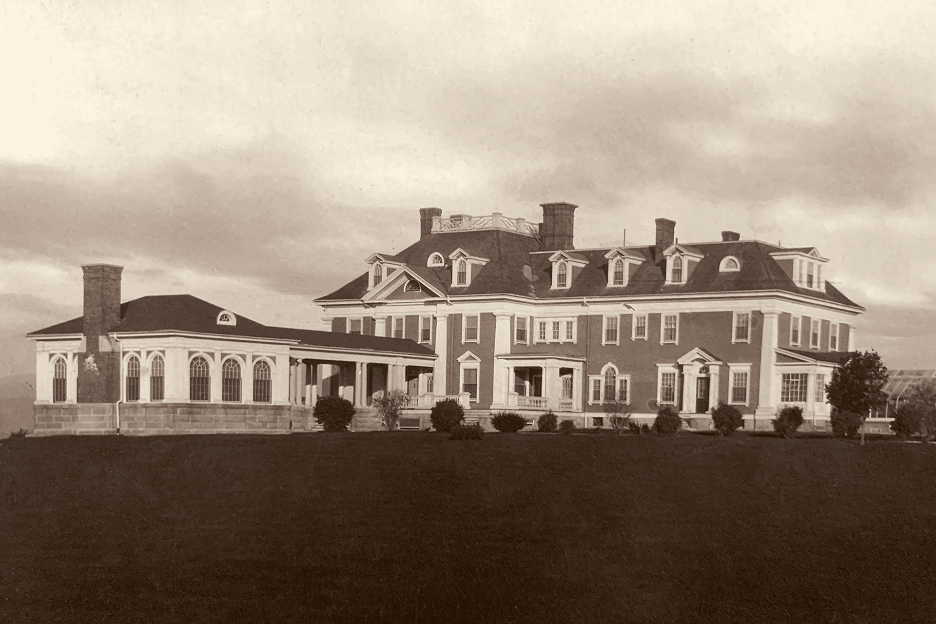 A large historic mansion with multiple gables and a porch, set on a landscaped lawn.