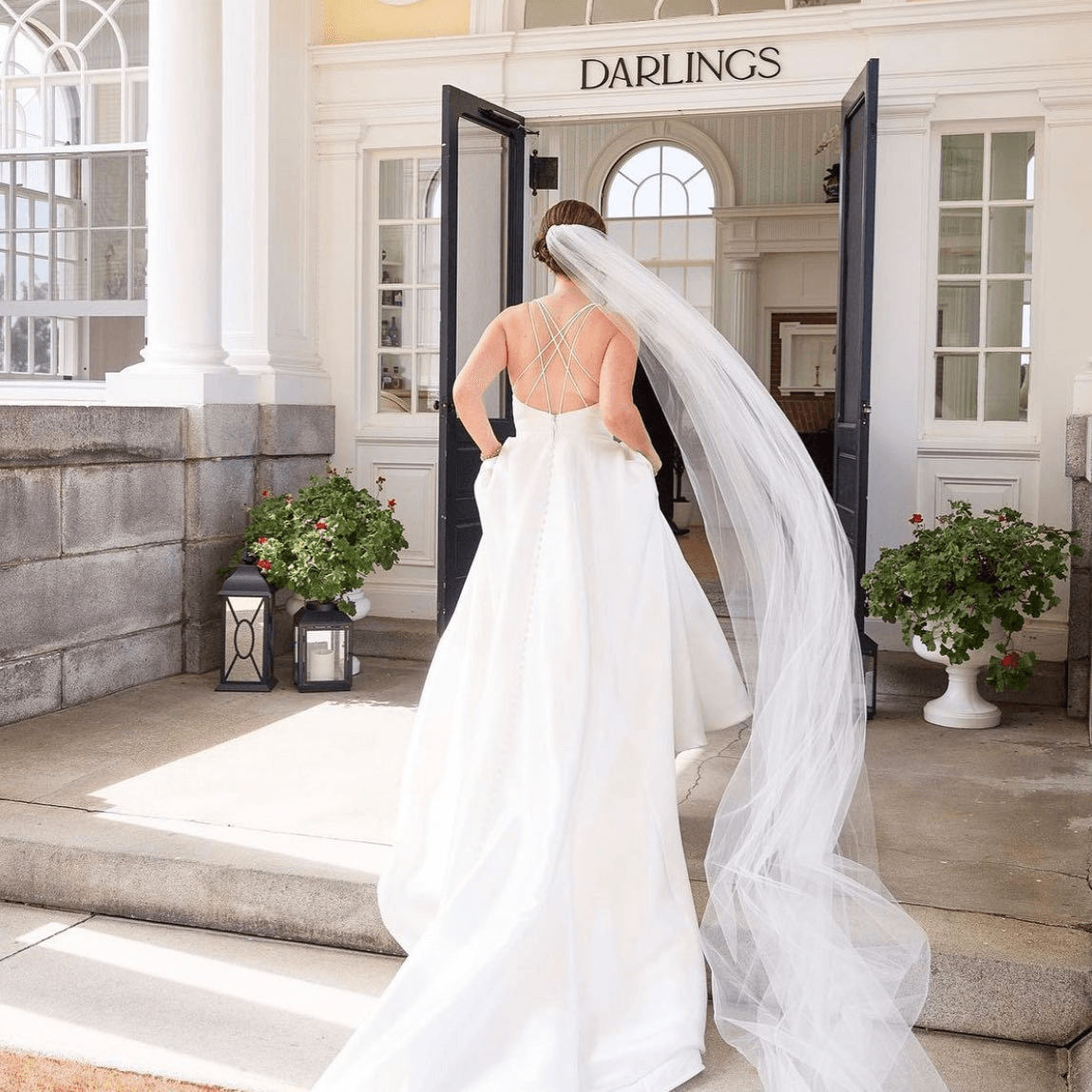 A bride in a flowing white gown and veil walks towards a doorway labeled "Darlings."