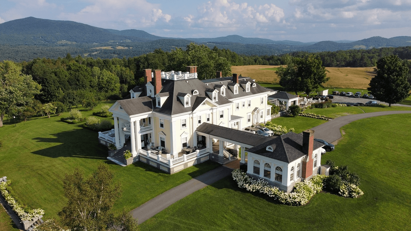 Aerial view of a grand mansion surrounded by rolling hills and lush greenery.