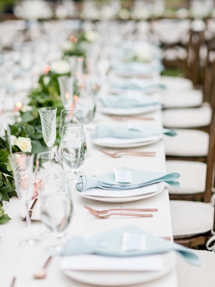 A elegantly set table featuring blue napkins, glassware, and decorative greenery.