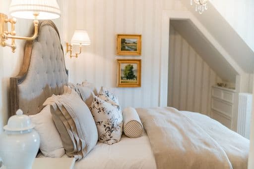 A cozy bedroom with a tufted headboard, soft bedding, and framed paintings on the wall.