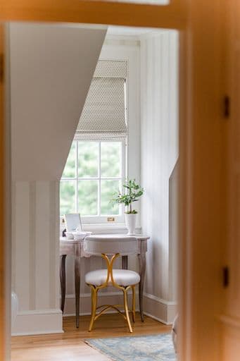 A cozy, well-lit nook featuring a small desk, a stylish chair, and a potted plant by a window.