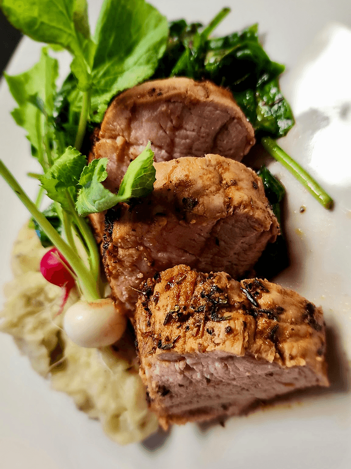 Sliced pork tenderloin served with sautéed greens and creamy mashed potatoes.