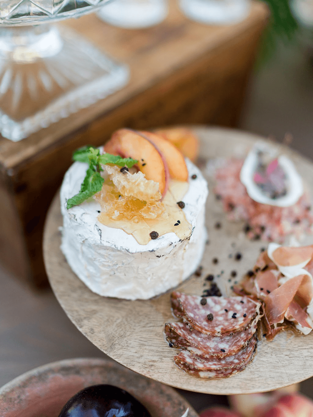 A wooden platter features cheese topped with fruit and honey, along with various cured meats.