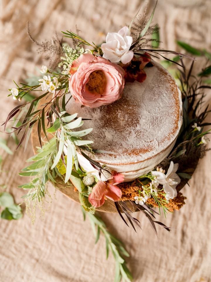 A rustic cake adorned with fresh flowers and greenery.