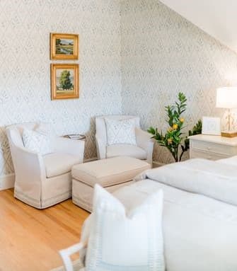 Brightly lit bedroom featuring white furniture, decorative artwork, and a potted plant.