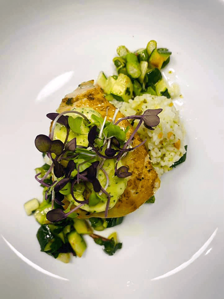 Grilled fish topped with green sauce and microgreens, served with rice and mixed vegetables.